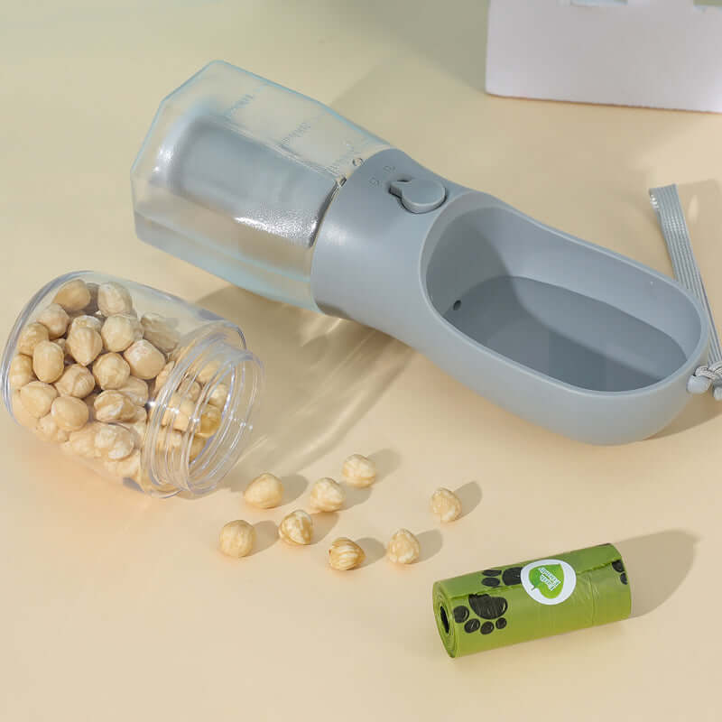 3 in 1 dog water bottle from PawKit with treat container and green roll of waste bags on a beige surface.
